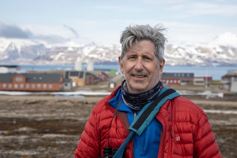 Portrett av ein mann i eit arktisk landskap. Ei busetnad i bakgrunnen.